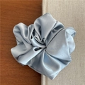 Detail of soft satin blue scrunchie showing smooth fabric texture and rich folds on book - Blue