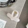 Detail view of a translucent pink heart-shaped hair claw clip with golden spring mechanism - Off White
