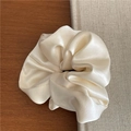 Detail of a cream satin scrunchie with rich pleats on a wooden table and book - Off White