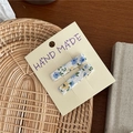 Detail von zwei floralen Stoff-Haarspangen auf einer Hand-Made-Karte auf Flechtwerk - Blau Blumen Rechteck Stil / Blau