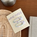 Set of two handmade purple floral fabric clips on a white card display over wood - Purple Flower Oval Style
