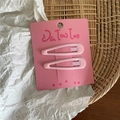 Close-up of two pink metal hair clips on a branded card over a textured rustic background - Light Pink