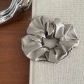 Detailed view of grey satin scrunchie with smooth pearl luster on a vintage book - Grey Green
