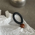 Détail d'un élastique spirale noir avec perle en résine marron sur surface en pierre - Bande Noire Avec Perle Rouge Brun
