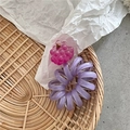 Detailansicht eines lila Spiral-Haargummis mit rosa Traubenanhänger auf einem Flechtkorb - Lila Trauben-Stil