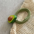 Close-up of a green velvet hair tie with a 3D avocado charm on a beige mesh background - Avocado