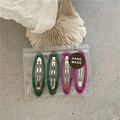 Close-up of four geometric resin hair clips in green and purple colors in packaging - Red and Green Oval