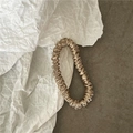 Close-up of champagne silk scrunchie with soft ripples on white and grey background - Champagne Gold
