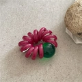 Detail of dark rose spiral hair tie with a large transparent green bead on stone texture - Rose Red Phone Cord (Green Bead)