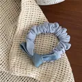 Dettaglio di uno scrunchie in denim celeste con cuciture gialle su maglia beige - Elastico Blu con Fiocco