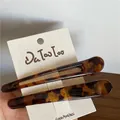 Dettaglio di due fermagli per capelli con stampa leopardata su carta di marca premium - Stile leopardato giallo bicolore