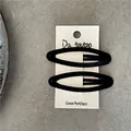 Pair of black velvet oval BB hair clips on a beige display card over a stone surface - Black