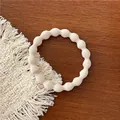 Detailed view of beige elastic hair tie with pearl-like wavy texture on a wooden surface - White