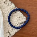 Detailed shot of a navy blue elastic hair tie with wavy texture on a woven coaster - Navy Blue