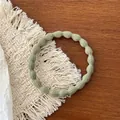 Detail of sage green ribbed elastic hair tie on a rustic wooden tabletop - Light Grey Green