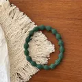 Close-up of a dark green elastic hair tie with a textured wave bead pattern on a wood surface - Dark Green