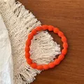 Detail of bright orange wave-patterned hair tie on a rustic wooden table setting - Orange