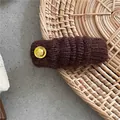 Nahaufnahme der dunkelbraun gestrickten Haarklammer mit einem runden goldenen Metallknopf - Kaffeebraun