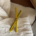 Close-up of a bright yellow velvet bow hair clip on a textured beige fabric surface - Yellow