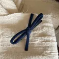 Close-up of navy blue velvet bow hair clip on beige textured fabric background - Blue