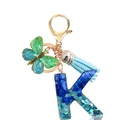 Detailed macro of resin letter K keychain with blue sequins, butterfly charm and blue tassel - Letter K