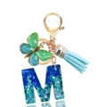 Close-up of resin letter M keychain with heart sequins, butterfly charm, and blue tassel - Letter M