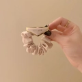 Dettaglio dello scrunchie in raso crema plissettato con placca logo triangolare oro - Beige