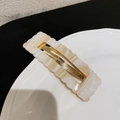 Detalle de pinza para el pelo de acetato a cuadros con bordes festoneados en plato de porcelana - Blanco