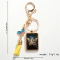 Detail of a butterfly keychain with yellow tassel and black rectangle charm with gold letter O - Letter O