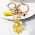 Detail of bee keychain with acrylic letter G, yellow tassel, and honeycomb pattern - Letter G