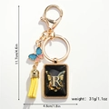 Close-up of golden letter R keychain with blue glitter butterfly and yellow tassel detail - Letter R