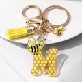 Detail of letter M acrylic keychain featuring honeycomb patterns and yellow tassel - M