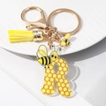 Macro shot of letter R keychain with honeycomb pattern, yellow tassel and pearl bee charm - Letter R
