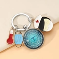 Detail of medical keychain with thermometer, nurse hat, and glass pendant on beige surface - Nursing Prayer Text Style (6)