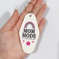Close-up of white motel style keychain with MOM MODE print held by hand - Rainbow MOM MODE