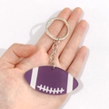 Dettaglio di un portachiavi a forma di football americano viola tenuto in mano - Palla da rugby