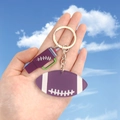 Détail macro des breloques de football violettes et gourde sur un porte-clés argent - Ballon de rugby