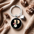 Detail eines Metall-Schlüsselanhängers mit Buchstabe P und rosa Blumen auf Seidenhintergrund - Buchstabe P