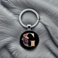 Detail of silver letter G keychain with floral patterns on polished black background - Letter G