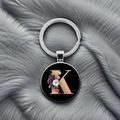 Detail of round keychain with golden letter K and elegant floral design on black background - Letter K