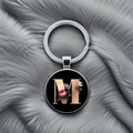 Detailed close-up of a round alphabet M keychain with floral patterns on grey faux fur - M