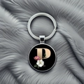 Detailed macro view of metal letter P keychain with floral patterns on grey plush surface - Letter P