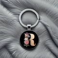 Detail of metal keychain with letter R and floral pattern on a grey plush surface - Letter R