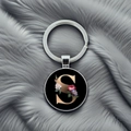 Close-up of a round silver keychain pendant featuring a gold letter S with floral design - S
