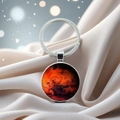 Silver metal keychain with red planet nebula pendant on elegant silk fabric background - Mars