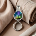 Close-up of metal nail clipper keychain featuring a scenic aurora borealis glass dome - Purple-Green Aurora and Black Forest