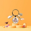 Vista macro di un portachiavi di laurea con ciondoli a forma di righello, taccuino e compasso - Tema Illustrazione Regalo Buon Compleanno Francese (5876366124548)