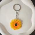 Dettaglio portachiavi a margherita gialla con petali realistici su un piatto di ceramica - Accessori color argento