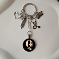 Detail of silver medical keychain with charms and a floral letter Q pendant on white surface - Letter Q