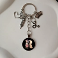 Detail of medical keychain with silver charms and floral letter R on a white background - Letter R